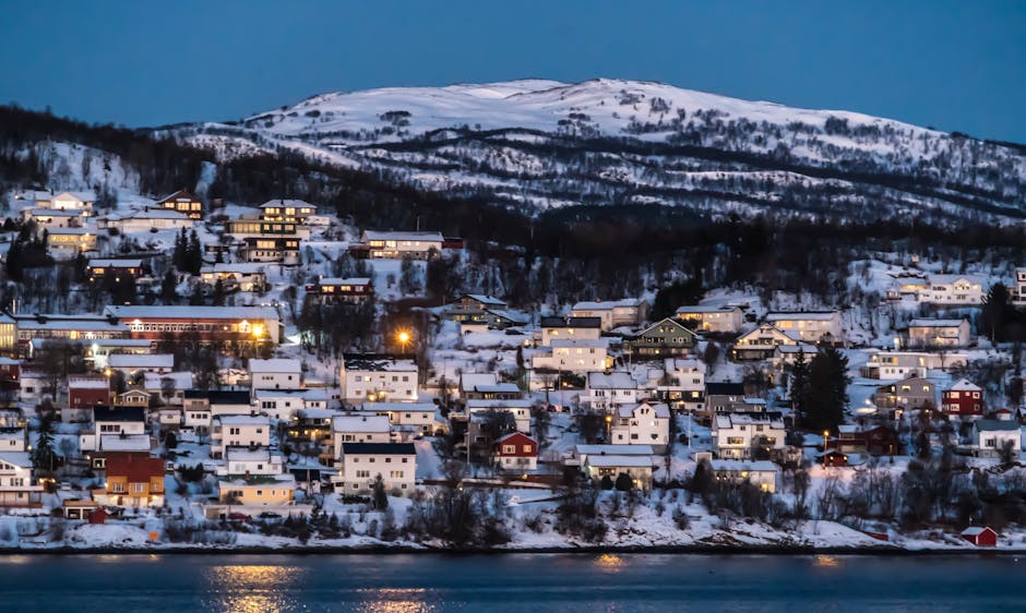 Charming snowy village set against Norwegian winter landscape illuminated at twilight.