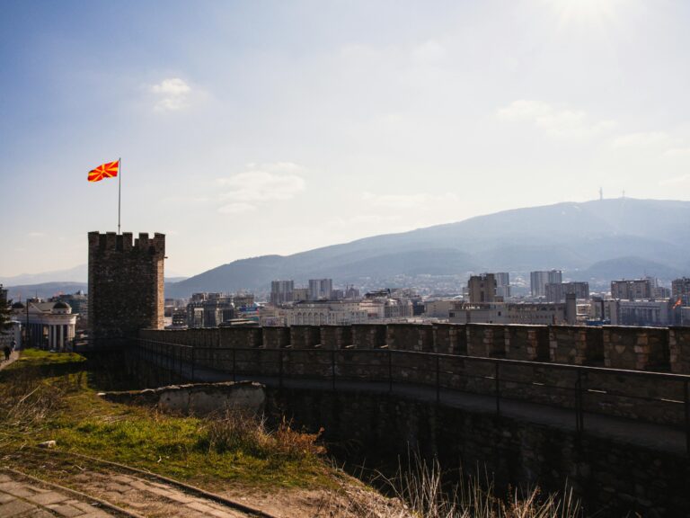 Panoramic view from Skopje Fortress with cityscape and Macedonian flag under clear blue sky.
