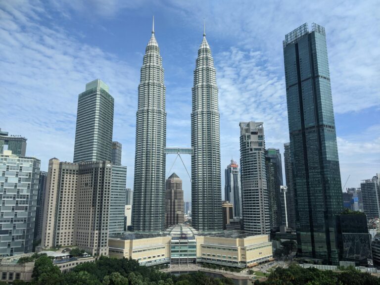 Panoramic view of the iconic Petronas Towers in Kuala Lumpur against a blue sky.