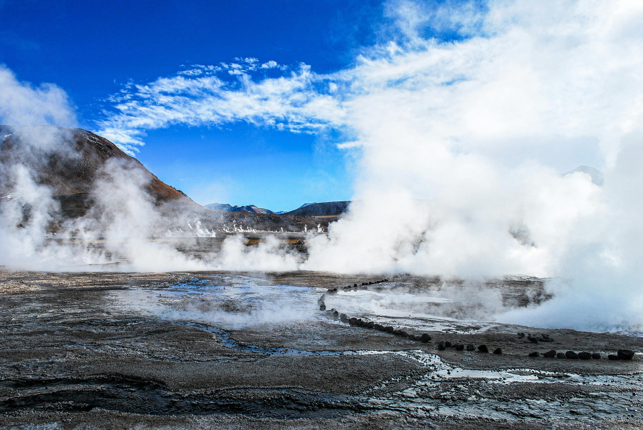 Captivating view of geothermal steam rising at El Tatio Geysers, Chile, under clear blue skies.