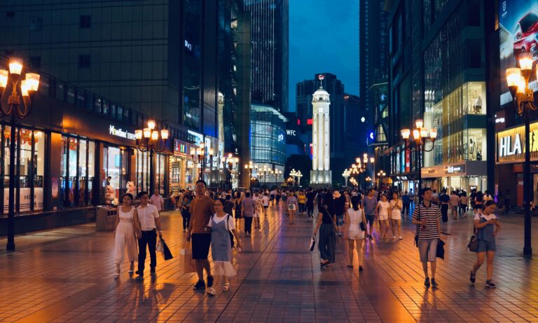 Bustling evening street scene in Chongqing's Jiefangbei Square with urban lights and shopping crowds.