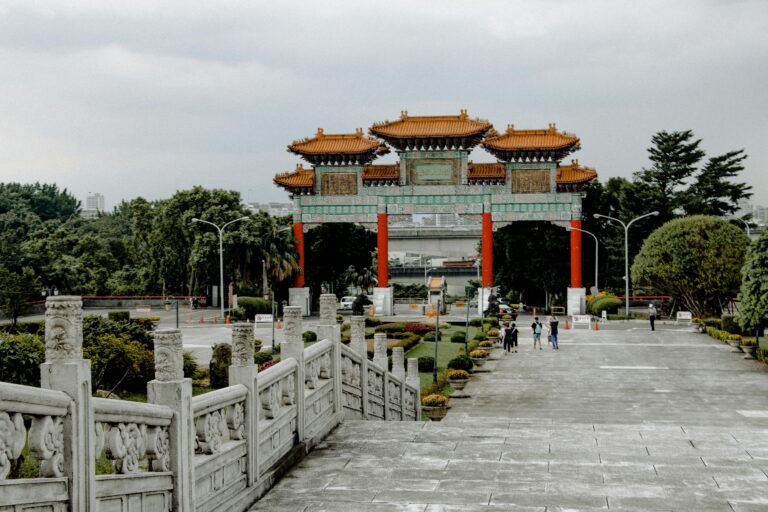 Captured traditional Chinese gate surrounded by lush greenery and tourists in a scenic city park.