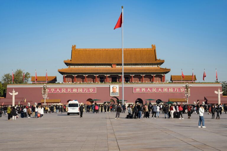 Crowds gather at the iconic Forbidden City Gate in Tiananmen Square, Beijing, under a clear sky.
