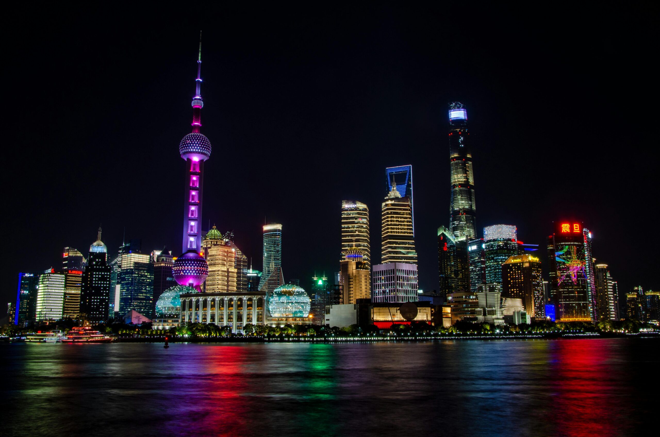 Vibrant night view of the Shanghai skyline featuring the Oriental Pearl Tower and colorful reflections.