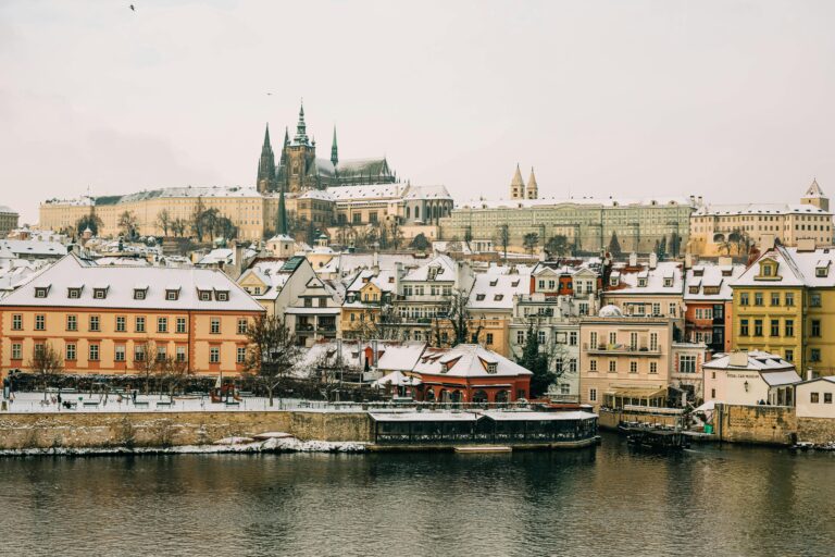 Picturesque winter scene of Prague Castle and Vltava River showcasing historic architecture under snow.