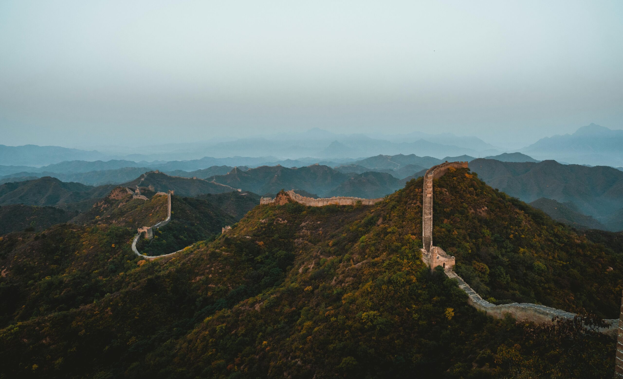 Scenic aerial view of the Great Wall of China stretching across rugged hills at dusk.