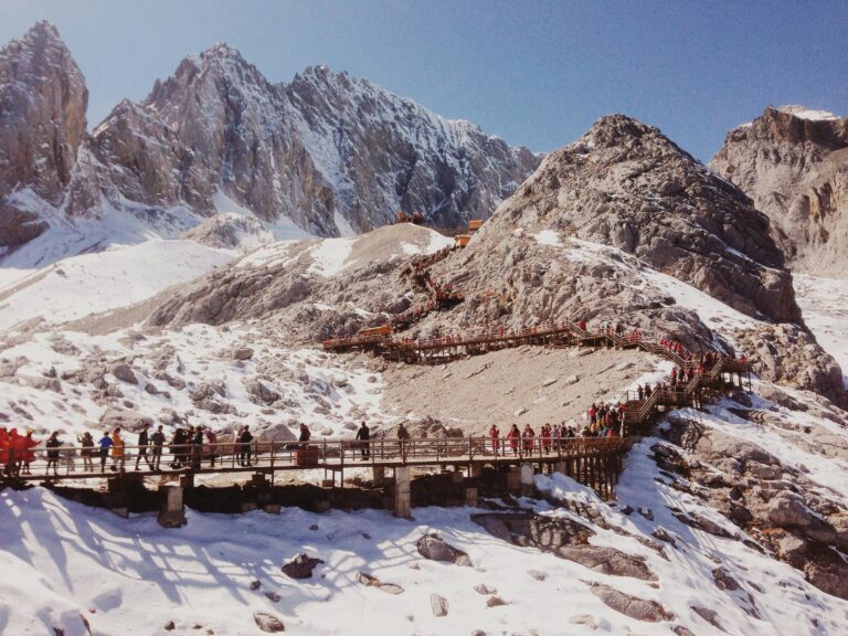 Tourists hiking wooden bridges amidst snowcapped peaks in Lijiang, China.
