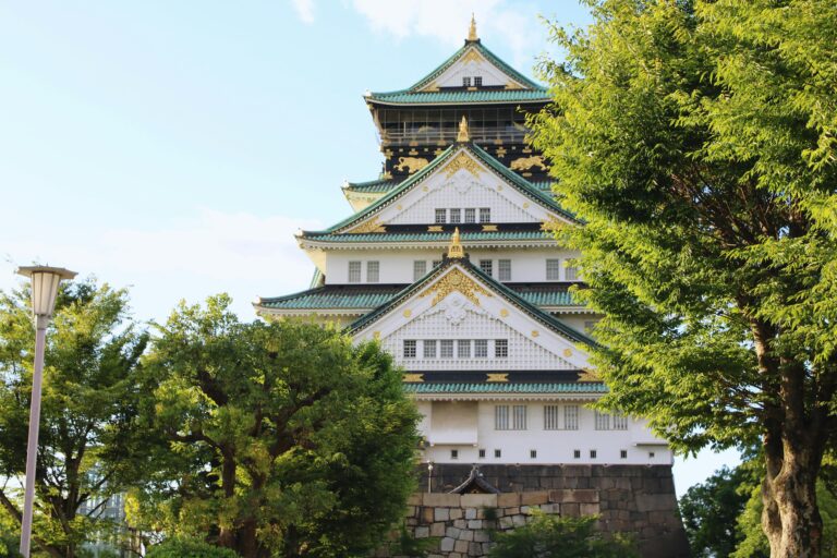 Explore the architectural beauty of Osaka Castle surrounded by lush greenery on a sunny day.