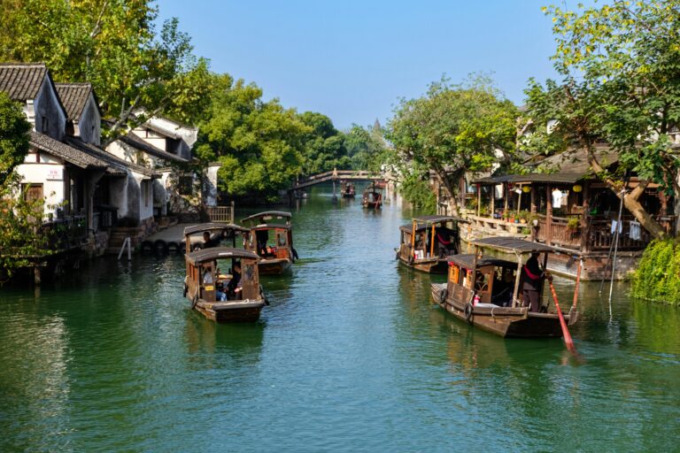 Traditional wooden boats ply the canals of a scenic Chinese water town surrounded by lush greenery.