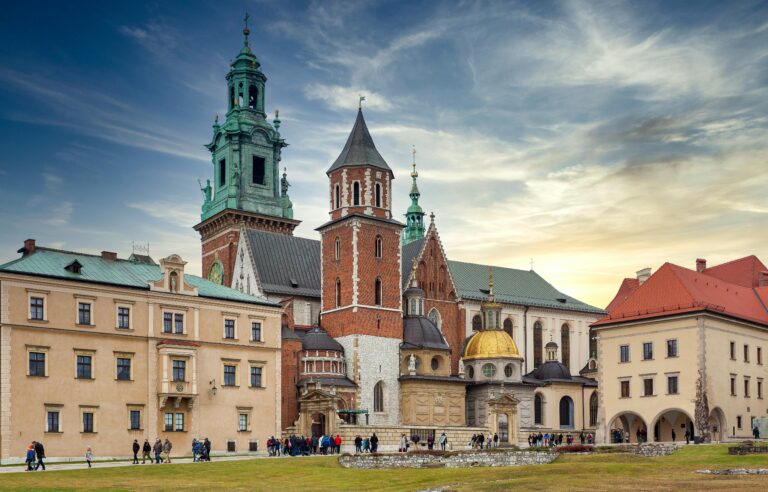 Traditional aged buildings and ancient Wawel Cathedral with various towers located on hill in Krakow against cloudy blue sky at sunset