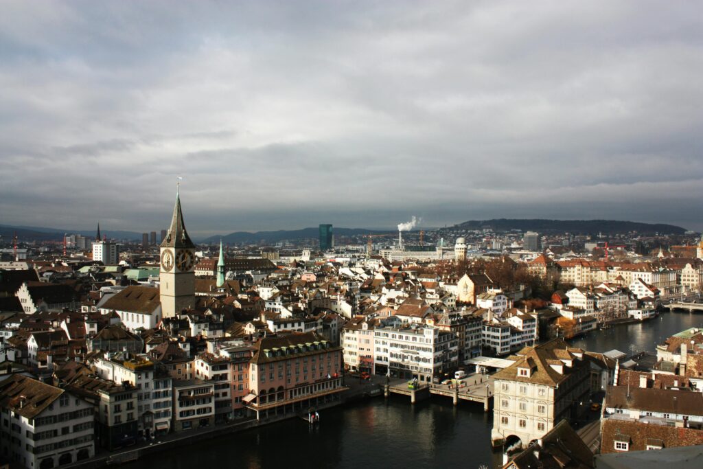 Explore a stunning aerial view of Zurich's historic cityscape with clock towers and canals under a cloudy sky.