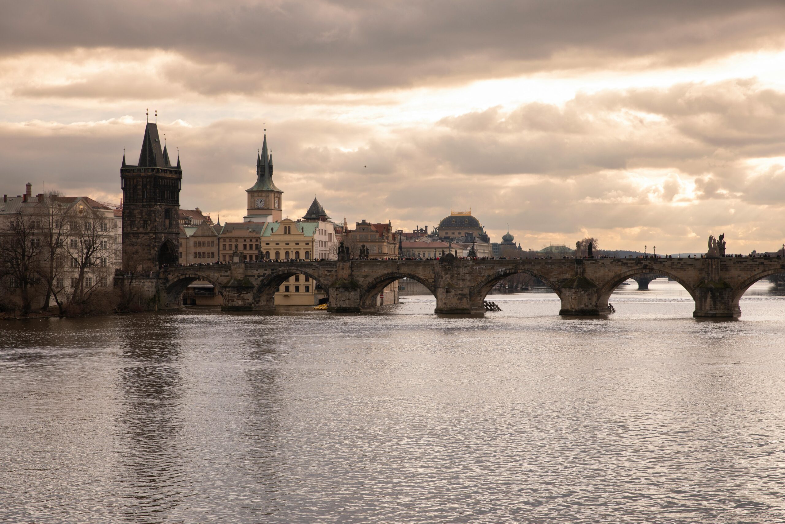 Scenic view of Charles Bridge in Prague over Vltava River with dramatic sky.
