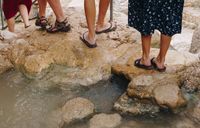 Travelers in sandals traverse rocky terrain in Ein Gedi's striking natural landscape.