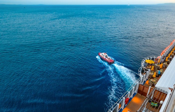 Aerial view of a luxury cruise ship with a small boat on a vast ocean at sunset.